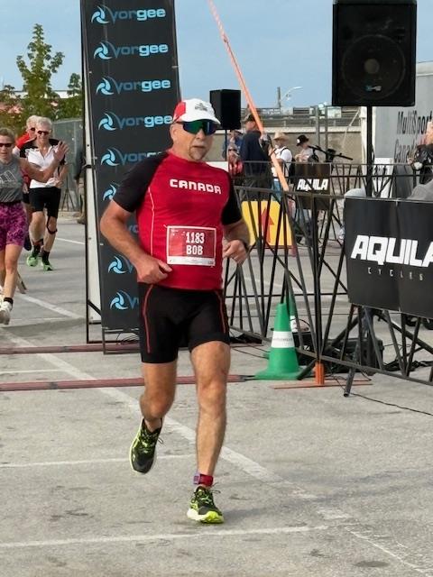 Bob Berezowski crossing the finish line at a duathlon wearing bib number 1183, embodying the athletic resilience and strength training philosophy he shared with clients throughout his 35-year career at the Toronto Athletic Club