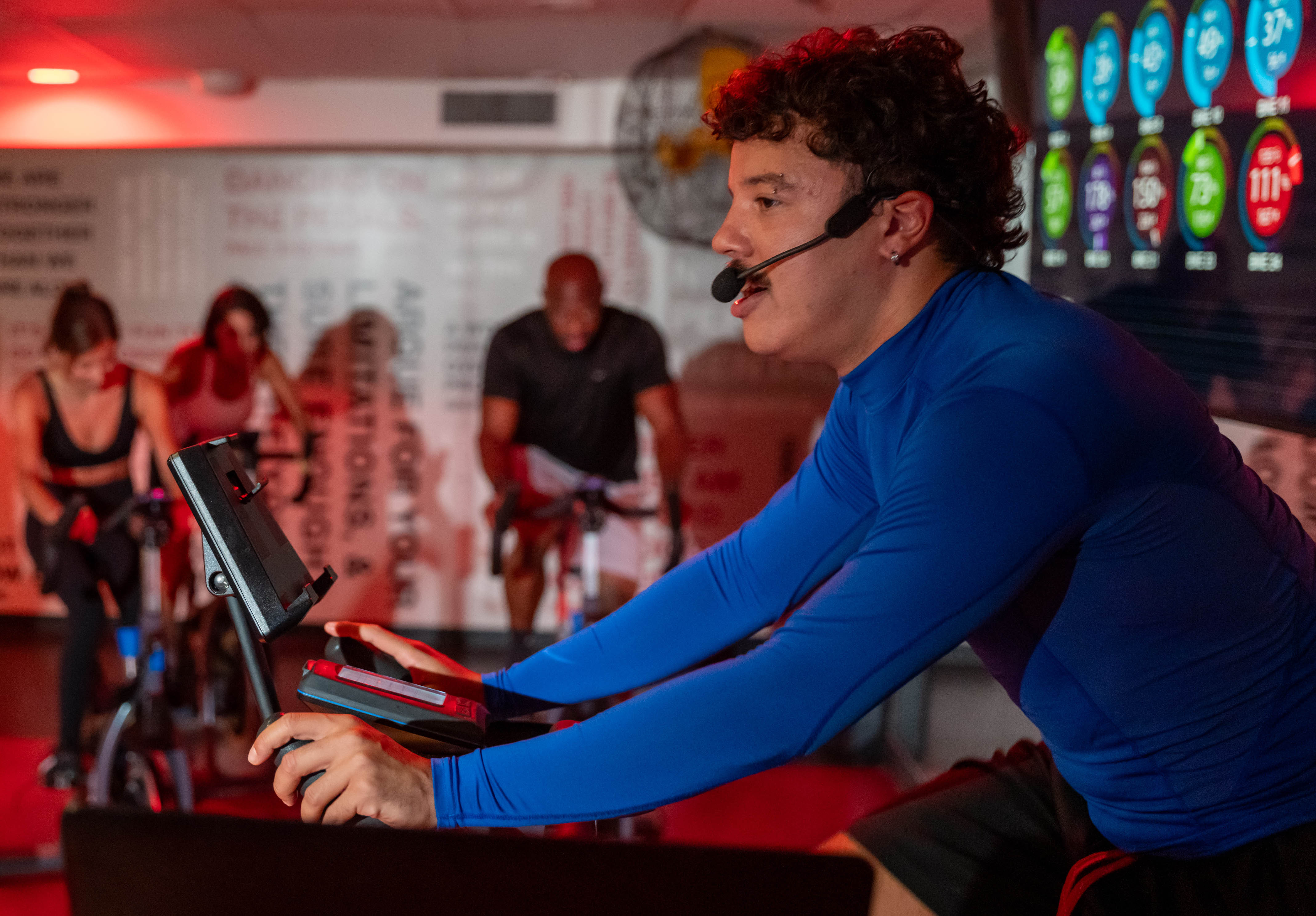 Male cycling instructor leading an A-Ride class in the Adelaide Club's Ride Studio, with the Stages technology on the screen in the background
