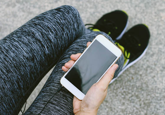 Close-up of the hand and legs of a woman in athletic gear, holding her phone - screen facing up - in her hand
