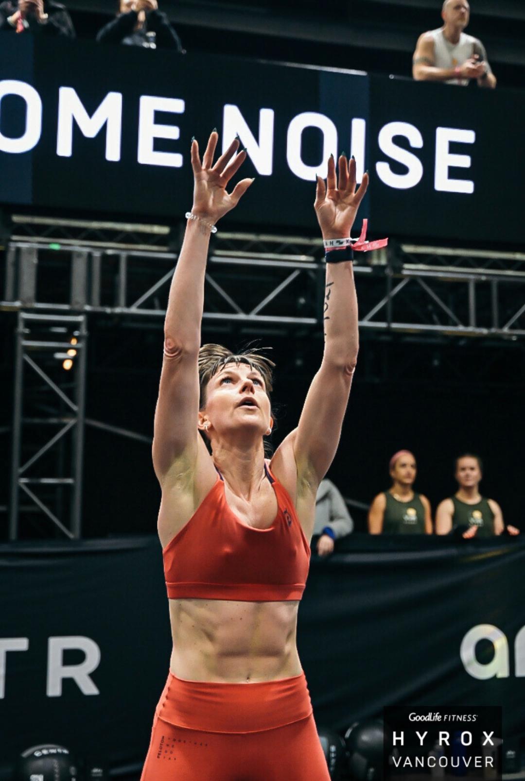 Athlete in red sports attire with arms raised celebrating at an indoor fitness competition in Vancouver.