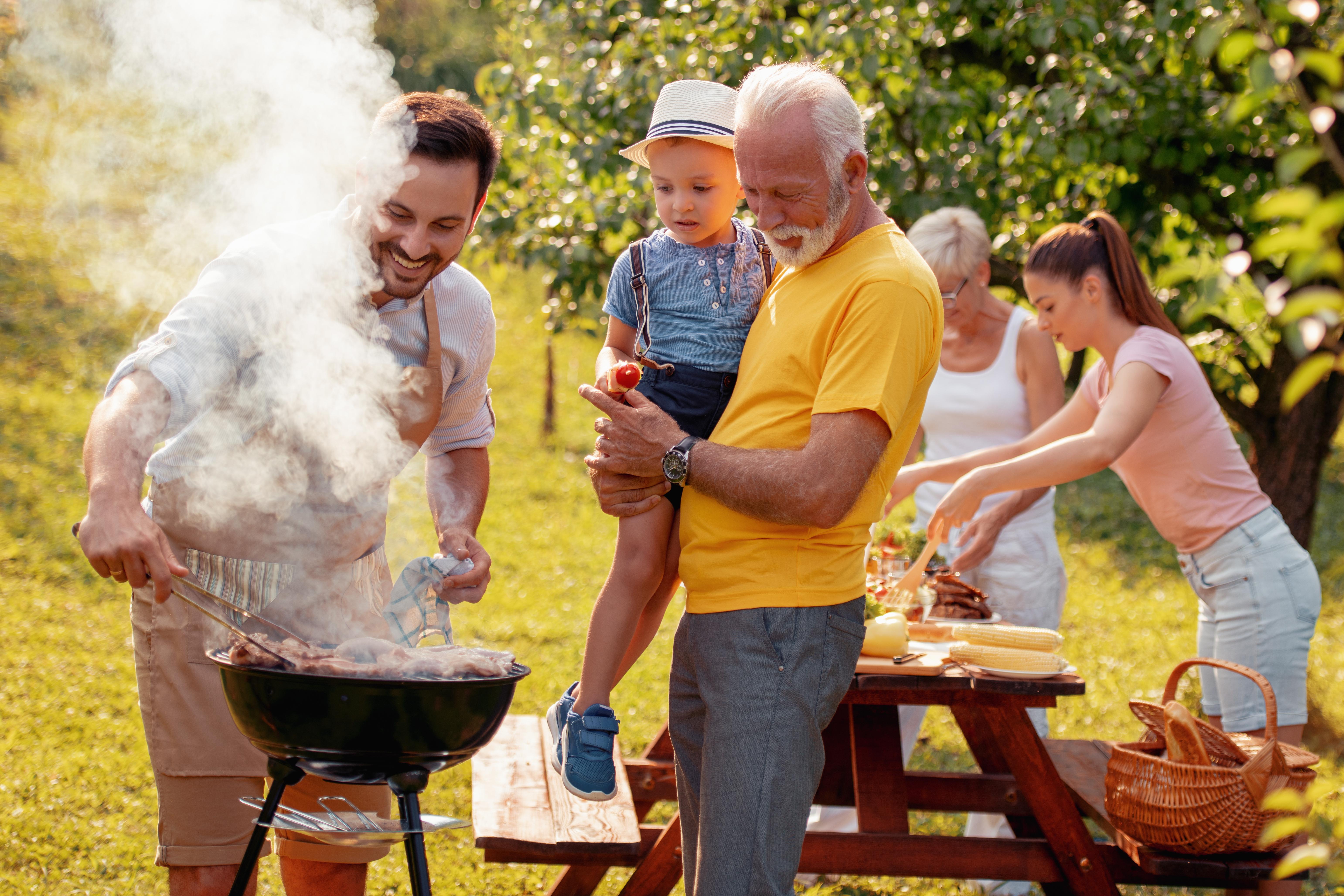 Multi-generational family enjoys a backyard barbecue picnic together on a sunny day.