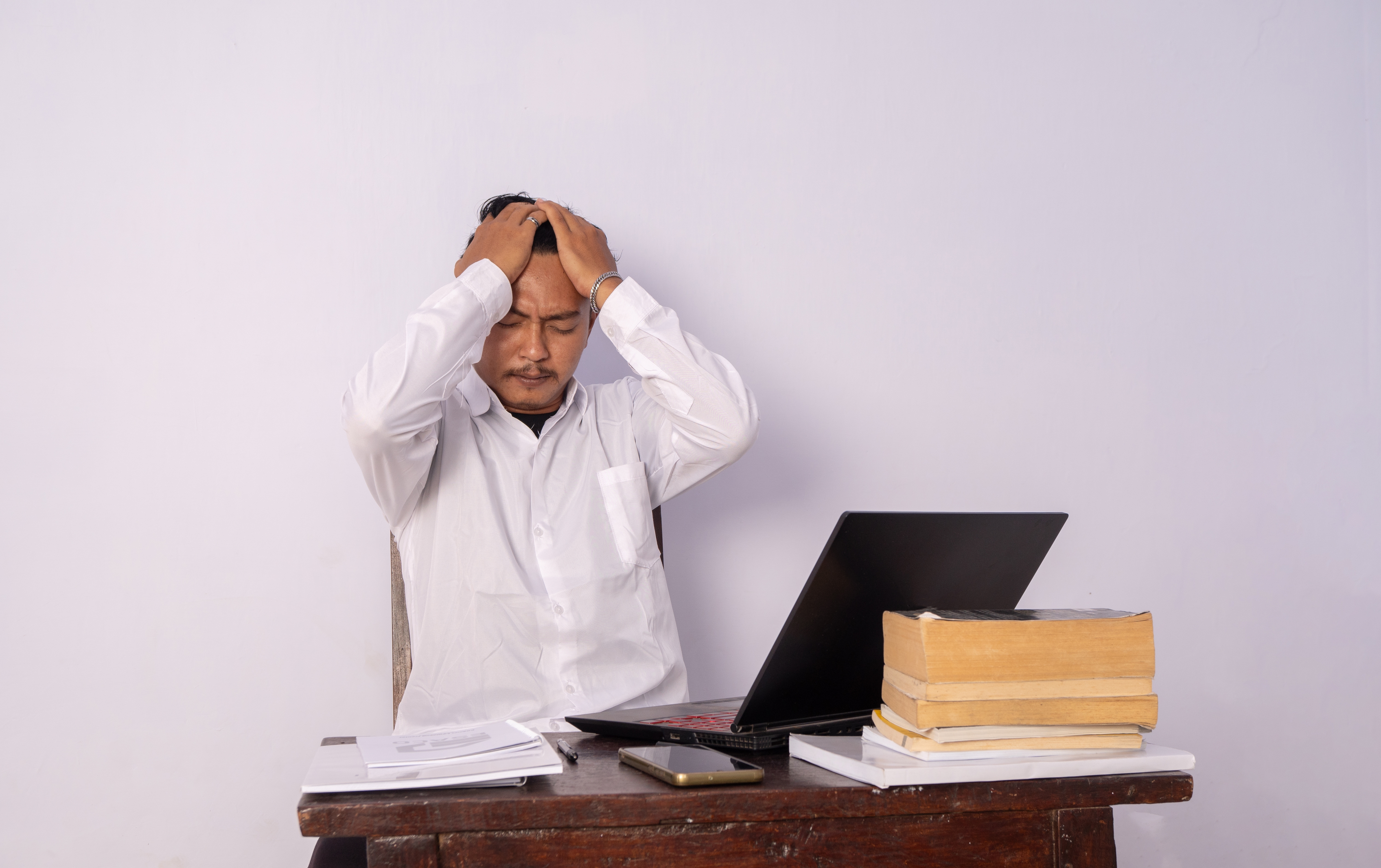 Stressed man with hands on his head sitting at a desk with a laptop